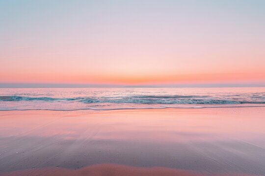 Waves gently roll onto a peaceful beach as the sky is painted in delicate shades of pink during sunrise.