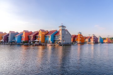 The tranquil lake is surrounded by houses painted in a variety of vibrant colors, creating a...