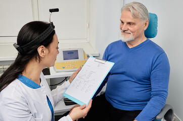 Experienced audiologist doing consultation for senior man patient with hear problems at audiology...