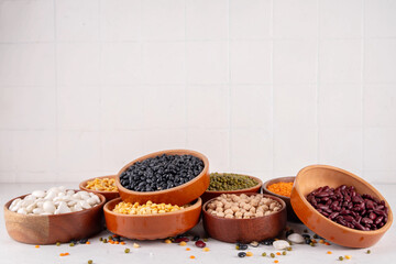 Various dried  beans, lentils, mung, chickpea, pea  assortment in wooden bowls. Legumes on white table top view. Vegan protein sources food, copy space