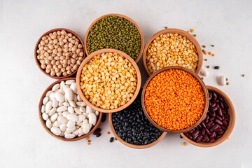 Various dried  beans, lentils, mung, chickpea, pea  assortment in wooden bowls. Legumes on white table top view. Vegan protein sources food, copy space