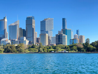 Fototapeta na wymiar View of Sydney downtown and its iconic buildings and skyscrapers at the distance. Australian city on the horizon. City skyline from the ocean shore. City harbour country, Australia.