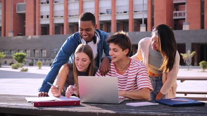 Group of multiracial happy teenage students using laptop, working on university assignment homework project at university campus. Meeting of diverse young classmates looking information on computer