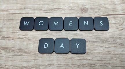 Women's day text on black buttons on wooden background, top view