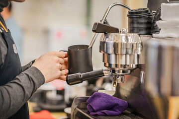 Professional barista working in bar whipping milk into foam for cappuccino coffee