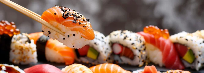 Foto op Plexiglas  Japanese salmon nigiri taken by chopstick and sushi pieces on the background. © Andrea Raffin