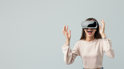 Engrossed woman with virtual reality headset reaching out as if to touch something only she can see on grey background