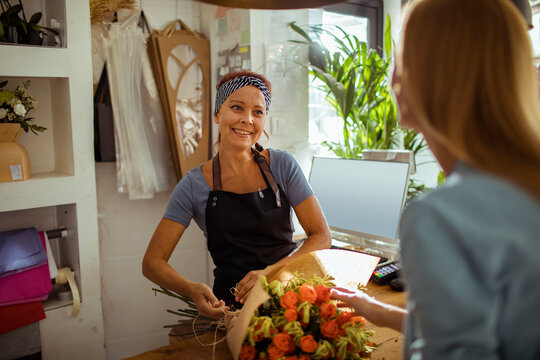 Smiling female florist finishing bouquet for customer in the flower store