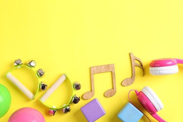 Baby song concept. Wooden notes, tambourines and toys on yellow background, flat lay. Space for text