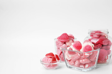 Different yummy pink candies in glass jar and bowls on white background, space for text