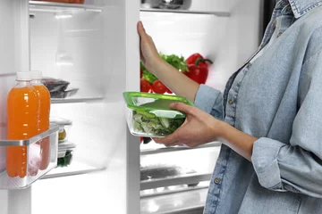 Poster Young woman taking container with vegetables out of refrigerator, closeup © New Africa