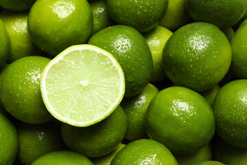 Whole and cut fresh limes with water drops as background, top view
