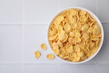 Breakfast cereal. Tasty crispy corn flakes in bowl on white tiled table, top view. Space for text