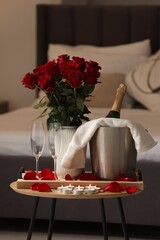 Honeymoon. Sparkling wine, glasses and bouquet of roses on wooden table in room