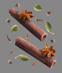 Cinnamon sticks and other aromatic spices falling on grey background