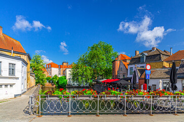 Predikherenbrug stone bridge across Groenerei Green Canal with metal fence with flowers pots, embankment in Brugge old town, medieval buildings in Bruges city historic centre, West Flanders, Belgium