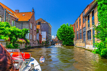 Bakkersrei water canal with tourists boat, Mariabrug bridge and medieval buildings walls with green plants in Brugge old town district, Bruges city historical center, West Flanders province, Belgium