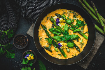 Omelette with green asparagus, basil and herbs on black background, top view