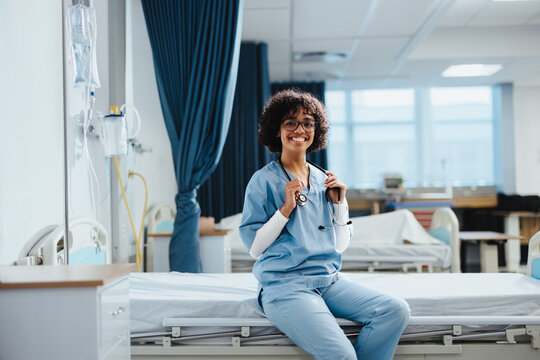 Medical doctor in training sits on a hospital bed, wearing scrubs and a stethoscope