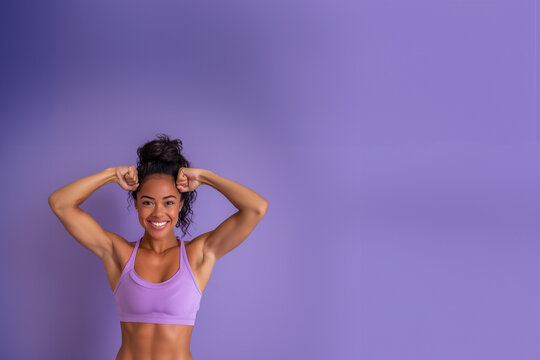 femme métisse, aux cheveux attachés, habillée en tenue de sport qui montre ses muscles très volumineux, dans une posture de bodybuildeuse, sur un fond violet avec espace négatif pour texte copyspace.