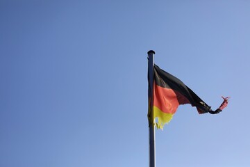 broken torn disastrous German flag on a flagpole in front of a blue sky with open space