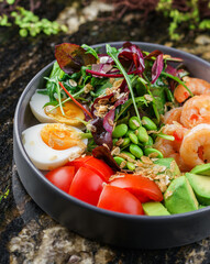 Buddha bowl salad with shrimps, arugula, spinach, avocado, tomatoes, green edamame beans, eggs on marble background. Healthy salad food, dieting, top view