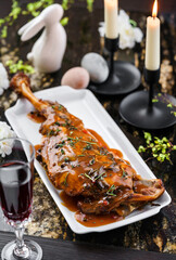 Baked lamb thigh leg, delicious meat for holiday with sauce and herbs on marble table with easter...