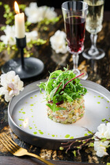 Salad Olivier with salmon, greens and avocado on marble background with decoration, flowers and wine glasses. Holiday food, top view