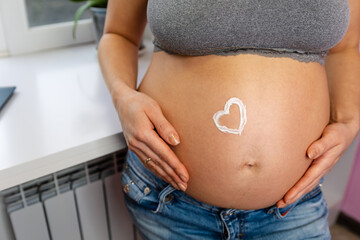An expectant mothers tender moment, cradling her growing belly adorned with a white heart,...
