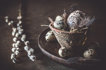 Easter decoration: rustic flower pot with natural quail eggs and feathers on a dark wooden plate...