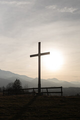 Religion theme, view of catholic cross silhouette, with fantastic sunset and mountains as background. Toned image