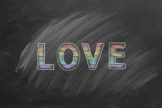 The word love is written with chalk on a blackboard. LGBT, LGBTQIA rights and gender equality concept. Pride month. Declaration of love, acceptance of feelings, giving love.