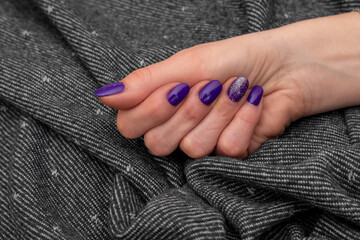 Purple well-groomed woman's hand resting on a uniform gray towel. Purple glitter nail polish with freshly applied. Beautiful manicured hand. Selective focus and Copy space.