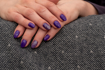 Fototapeta premium Well-groomed woman's hands resting on a uniform gray towel. Purple glitter nail polish with freshly applied. Brilliant trilogy diamond ring. Beautiful manicured hands. Selective focus and Copy space.