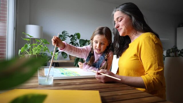 grandmother and granddaughter drawing with watercolor a painting at home happy