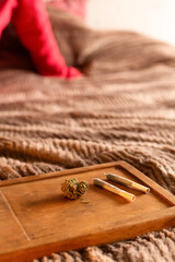 Close-up view of cannabis bud and pre-rolled joints on wooden tray against cozy background