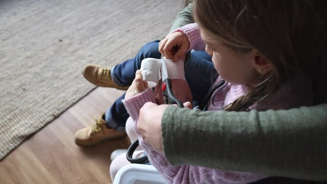 grandmother and granddaughter with first aid kit cutting a bandage at home on the sofa