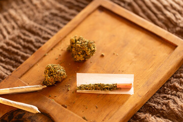 Hand-rolled marijuana joint on a wooden tray with cannabis buds and rolling paper