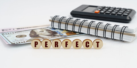 On a high surface lie a notepad, a calculator, dollars and wooden circles with the inscription - PERFECT