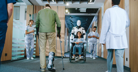 Fototapeta premium Helpful automated futuristic robot pushing wheelchair with young female patient in digitalized hospital. Useful digital bot serving in modern clinic helping people. Technological development.