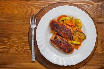 Beef cutlet with fried vegetables on a white plate on a deck table next to a fork. copy space