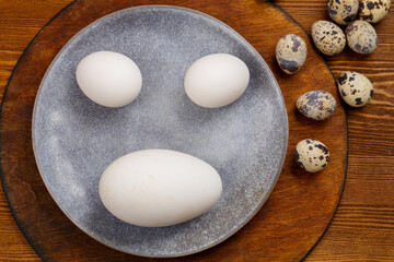Fototapeta na wymiar Chicken goose eggs on a gray plate on a wooden stand next to quail comparison