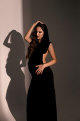 beautiful pregnant woman with dark hair in elegant clothes posing in studio