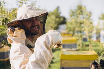 Happy smiling Indian Beekeeper in a uniform standing in apiary and holding bee on bees farm