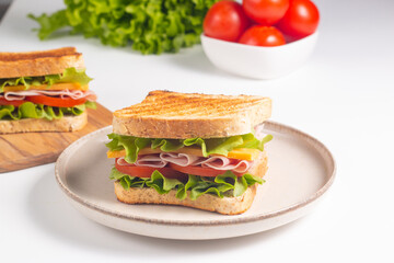 Close-up of two sandwiches with bacon, salami, prosciutto and fresh vegetables on rustic wooden cutting board. Club sandwich concept - 750911102