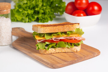 Close-up of two sandwiches with bacon, salami, prosciutto and fresh vegetables on rustic wooden cutting board. Club sandwich concept