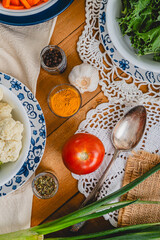 Close up of group of ingredients including a tomato, scallion, garlic, turmeric and pepper on vintage table setting