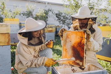 Couple of happy smiling beekeepers working with beekeeping tools near beehive at bee farm