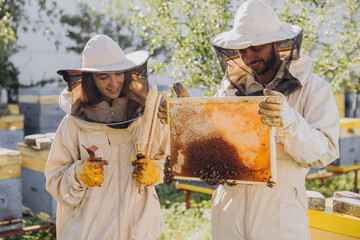 Couple of happy smiling beekeepers working with beekeeping tools near beehive at bee farm