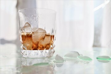   half empty fizzy soda with icecubes in a glass , highkey bright white background